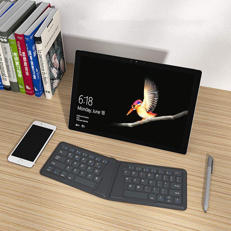 Folding Bluetooth keyboard compatible with Apple devices on desk with tablet, smartphone, books, and pen