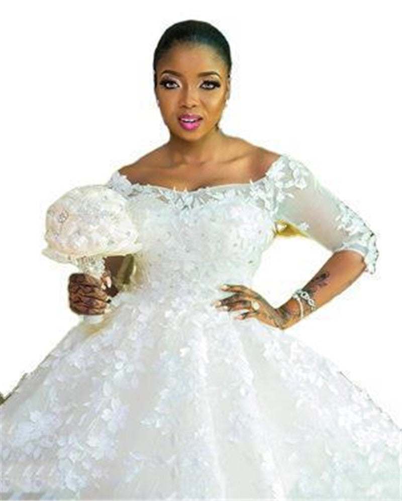 Pregnant woman wearing a white princess wedding dress with off-shoulder neckline and floral details holding a bridal bouquet