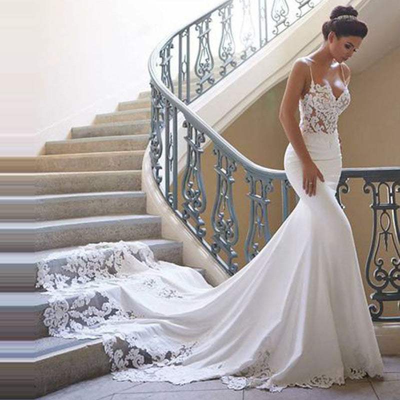 Bride wearing a pure white spaghetti straps lace bridal gown with a long train standing on stairs