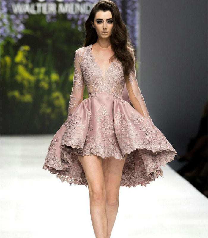 Woman wearing pink lace brocade short high-waist dress with deep V-neck and long sleeves on runway