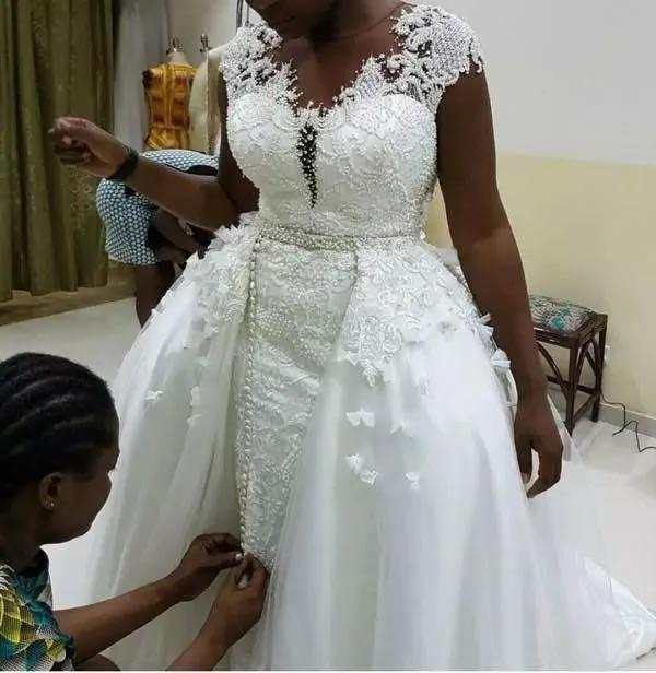 African mermaid detachable lace wedding dress in white linen with intricate floral lace detailing and a flowing skirt.