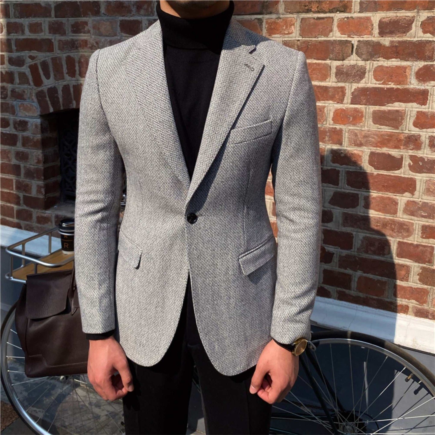 Gray thick textured suit jacket for men with single button and double slit back, styled casually over black turtleneck sweater.