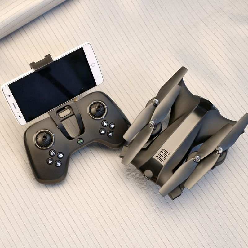 Folding drone remote control with smartphone holder and compact foldable quadcopter on a notebook background