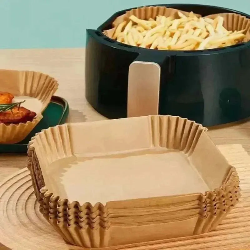 Stack of brown air fryer blotting paper sheets next to an air fryer with fries and food on paper liners