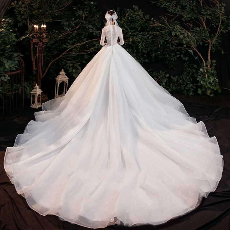 White bridal gown with long trailing skirt and sheer long sleeves in outdoor garden setting
