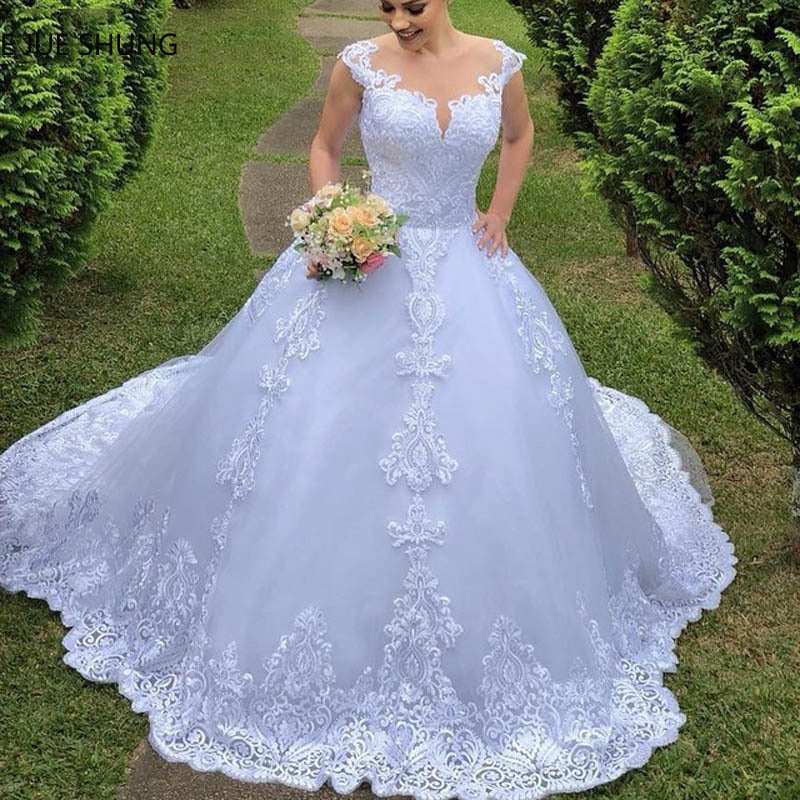 White vintage lace wedding dress with puff skirt, floral embroidery, and off-shoulder neckline, model holding bouquet outdoors