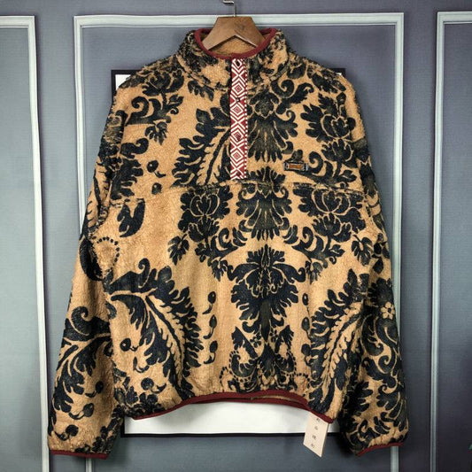 beige and black patterned fleece jacket with quarter zip and red trim hanging on wooden hanger