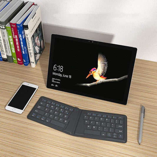Folding Bluetooth keyboard compatible with Apple devices on desk with tablet, smartphone, books, and pen