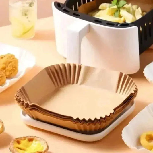 Stack of brown air fryer blotting paper sheets placed on a white tray next to an air fryer basket with cooked food and plates with fried snacks