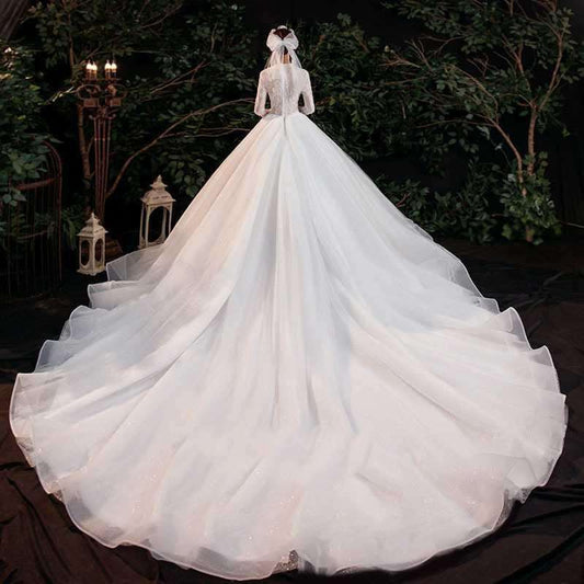 White bridal gown with long trailing skirt and sheer long sleeves in outdoor garden setting