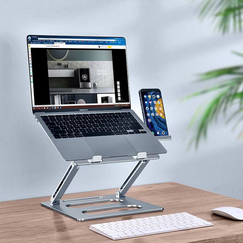 Adjustable metal laptop stand holding a MacBook and smartphone on a wooden desk with a keyboard and mouse nearby